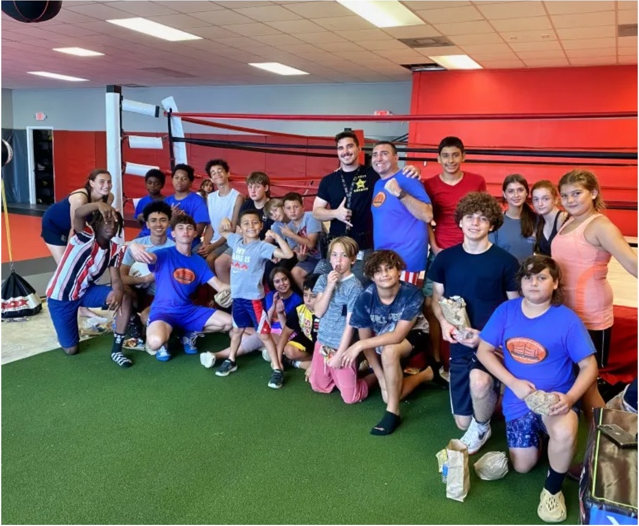 A group of young boxers and adults gathered in front of a boxing ring